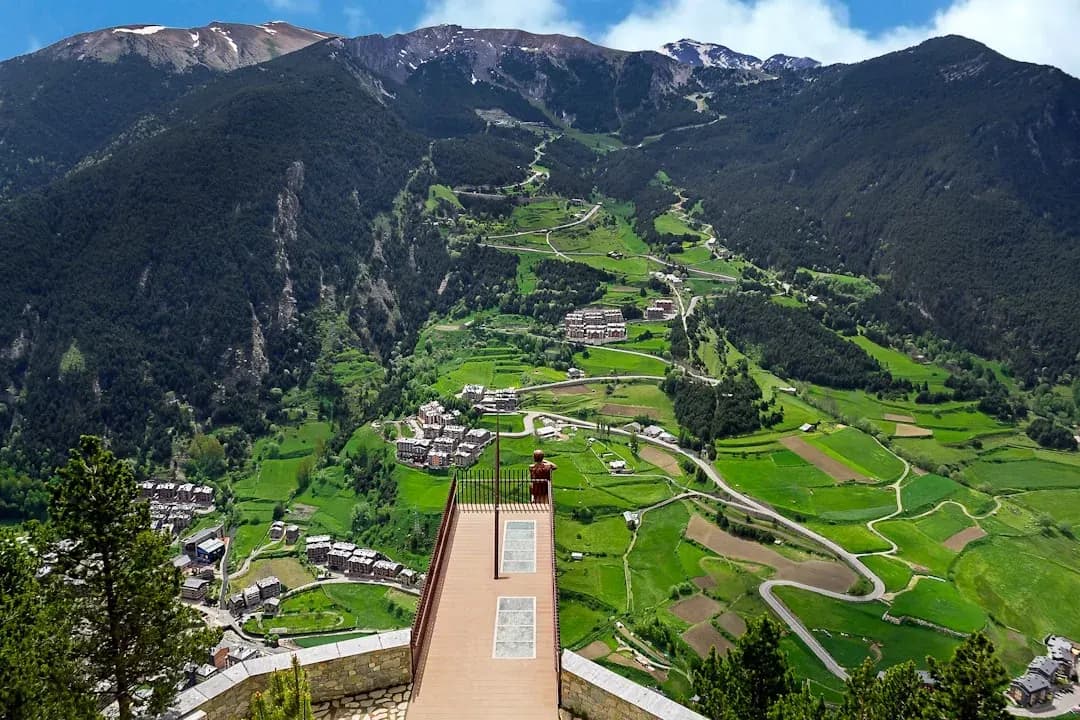 A freelance contractor at a desk in Andorra la Vella, invoices and a laptop in view, the Pyrenees rising through the window behind.