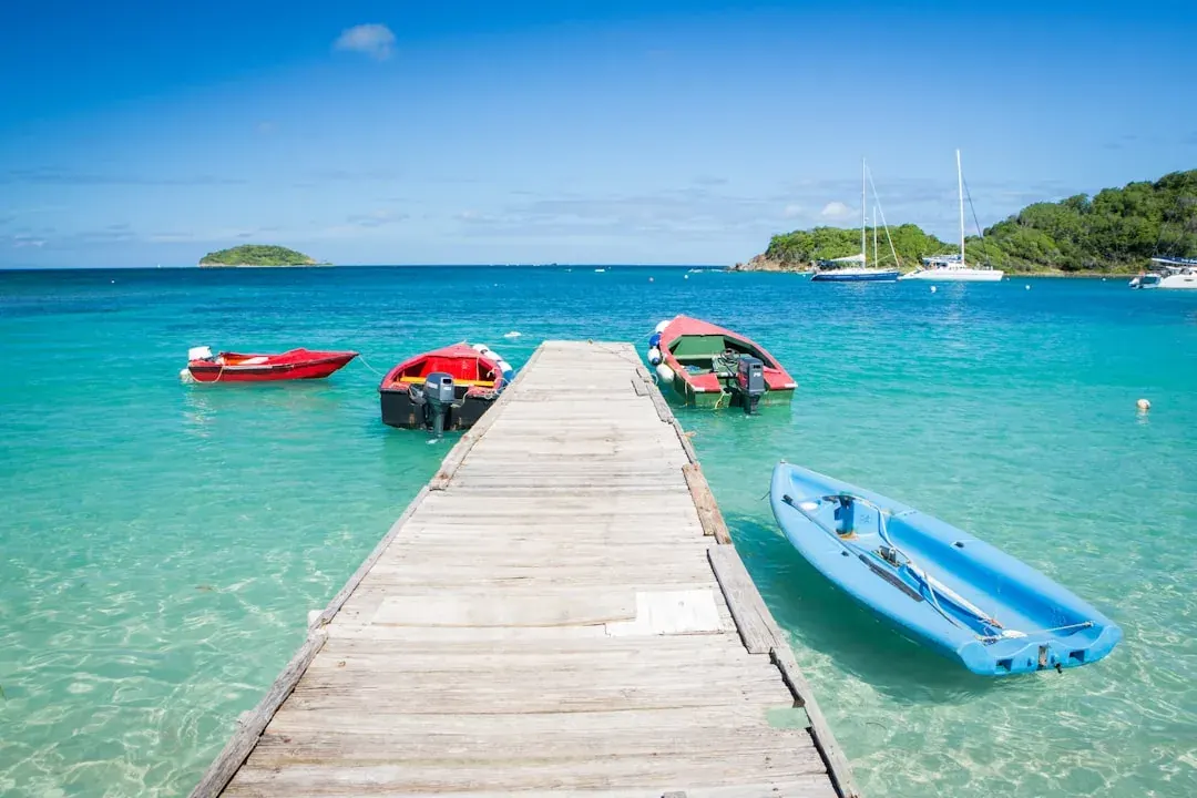 A warm wide view of English Harbour in Antigua at golden hour, fishing boats moored against the green hills of Nelson's Dockyard, with a freelance consultant's laptop and invoice on a table in the foreground.