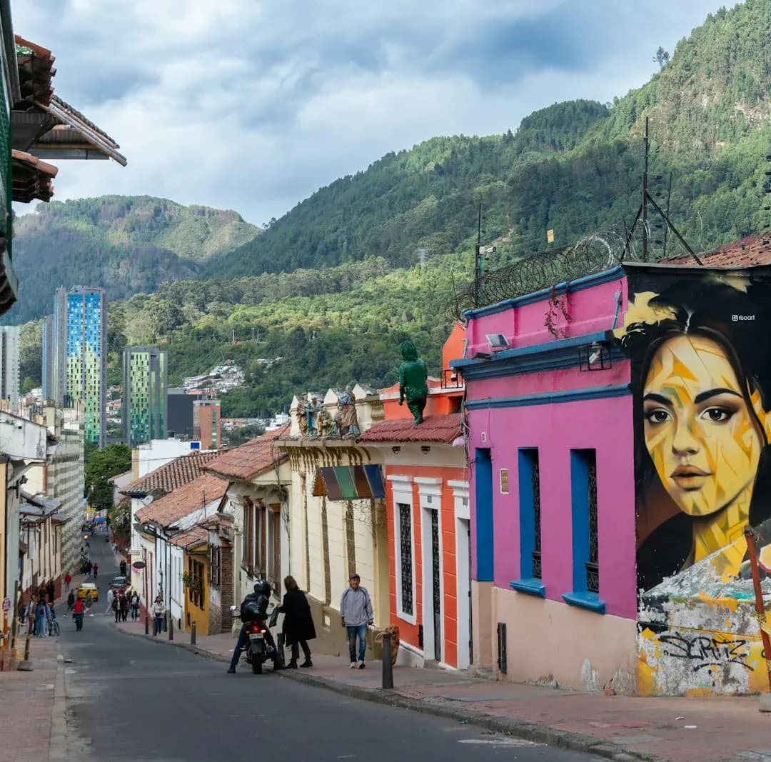 A wide illustration of Bogota at golden hour: the historic La Candelaria neighbourhood in the foreground, Monserrate mountain rising behind, and a clear amber sky above the city.
