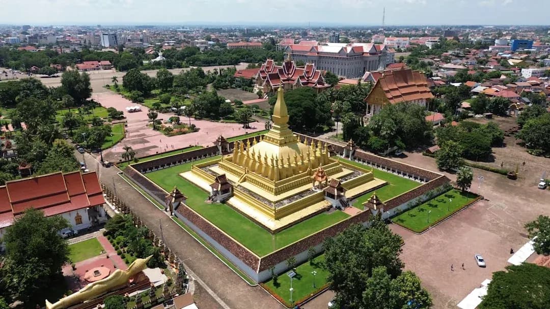 A freelance contractor in Vientiane working at a desk near a window, with the Mekong River and the That Luang temple spire visible in the warm afternoon light outside.