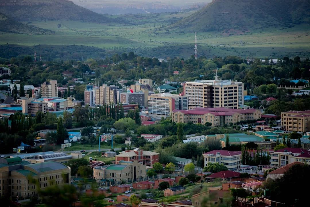 A contractor working at a desk near a window in Maseru, with the Maluti mountains visible in the distance and warm afternoon light filling the room.