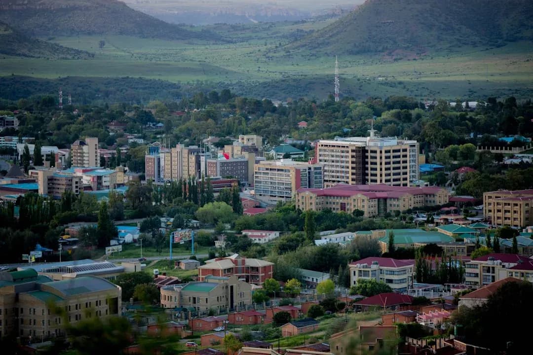 A contractor working at a desk near a window in Maseru, with the Maluti mountains visible in the distance and warm afternoon light filling the room.