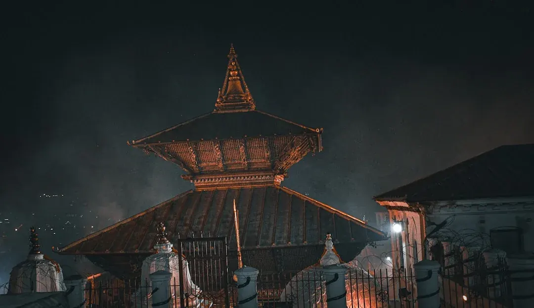 A warm illustration of Kathmandu at golden hour: temple rooftops and the Boudhanath stupa in the foreground, with the foothills rising behind the city under a soft amber sky.