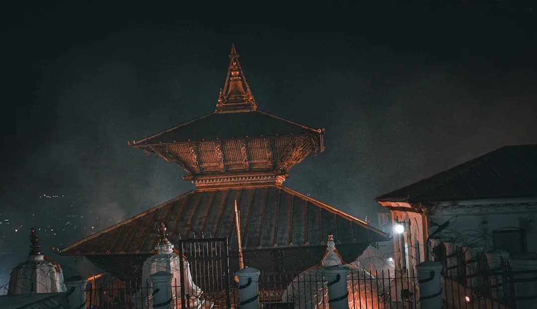 A warm illustration of Kathmandu at golden hour: temple rooftops and the Boudhanath stupa in the foreground, with the foothills rising behind the city under a soft amber sky.