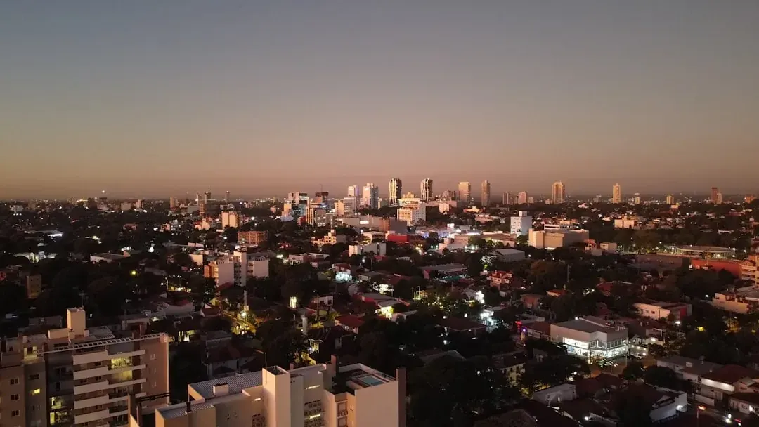 A warm illustration of Asunción at golden hour, the Paraguayan capital seen from the Paraguay river, with the Palacio de los López on the waterfront and a soft amber sky above.
