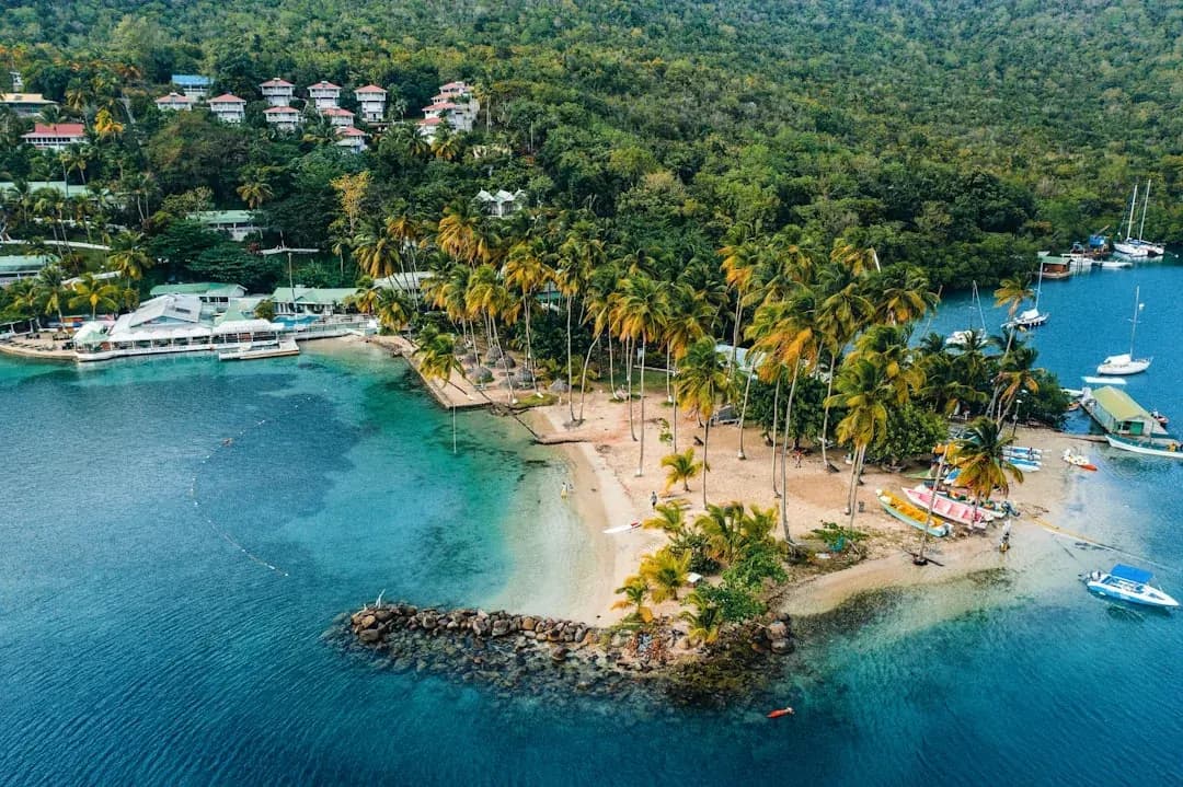 A warm view of Rodney Bay in Saint Lucia, sailboats on calm blue water against the green northern hills, with an open laptop and contractor invoice on a waterfront table.