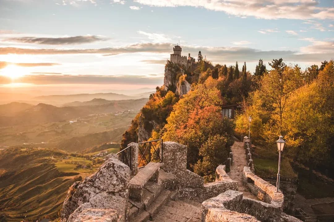 A contractor working at an outdoor table on a terrace in San Marino, with the three towers of Monte Titano and the medieval skyline visible in the afternoon light.