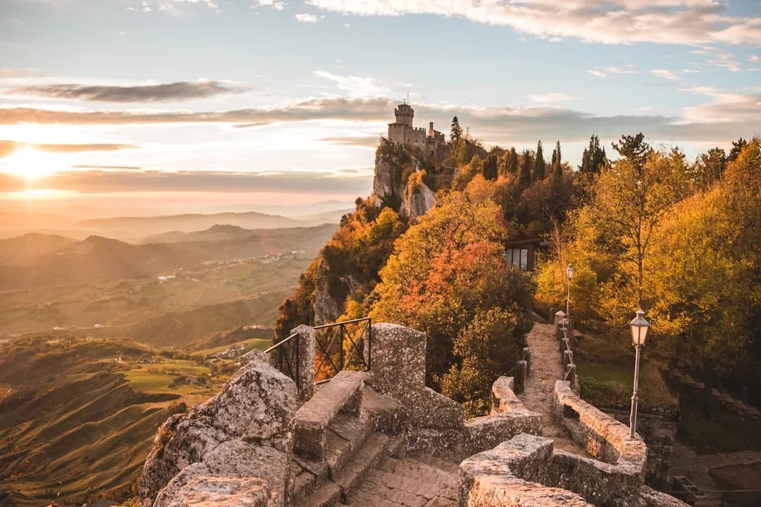 A contractor working at an outdoor table on a terrace in San Marino, with the three towers of Monte Titano and the medieval skyline visible in the afternoon light.