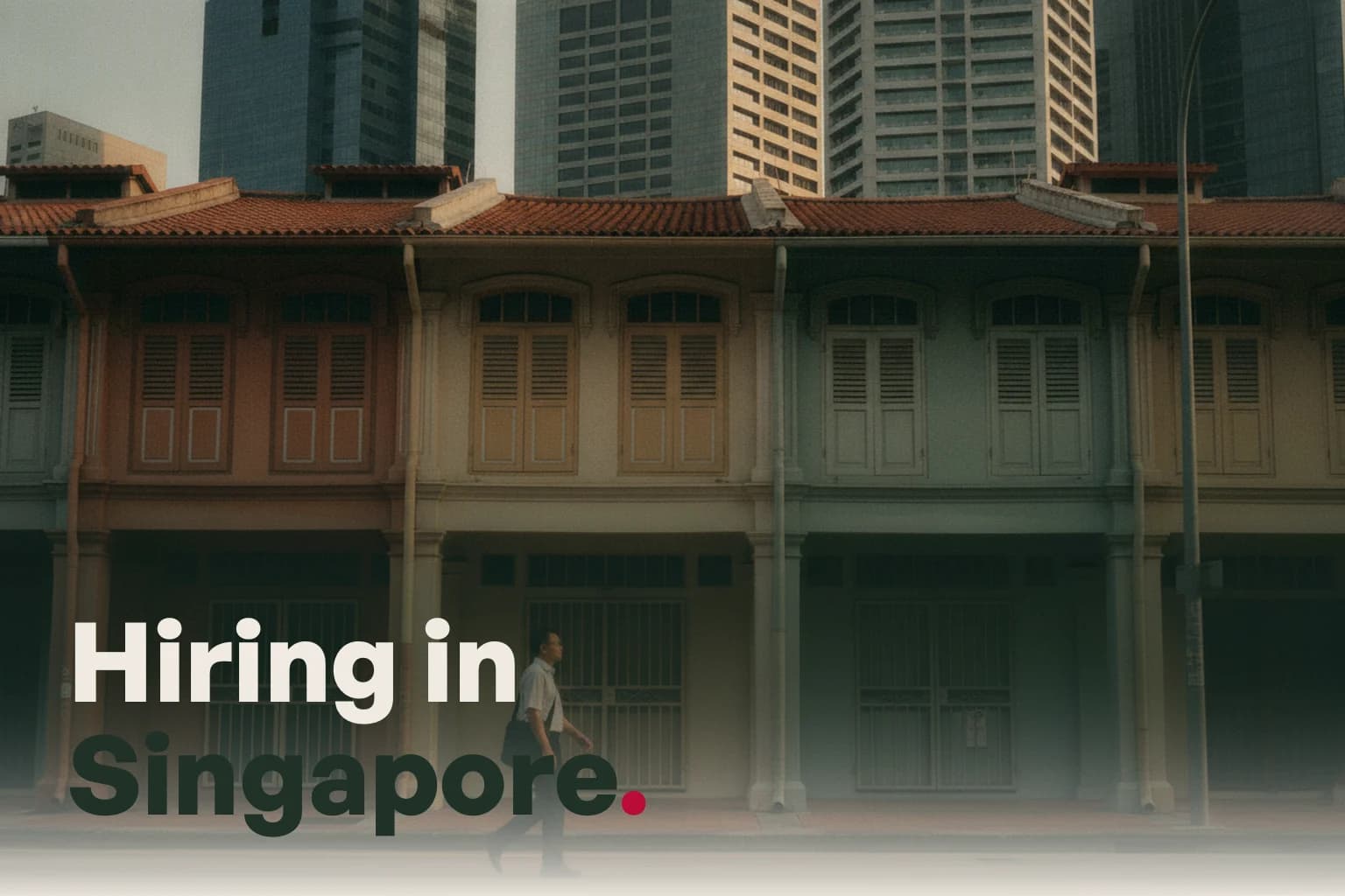A Singapore street of shophouses with towers behind in the early evening, with the line Hiring in Singapore.
