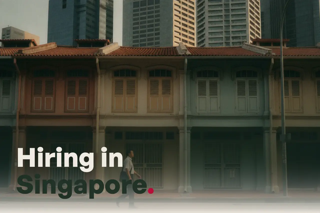 A Singapore street of shophouses with towers behind in the early evening, with the line Hiring in Singapore.