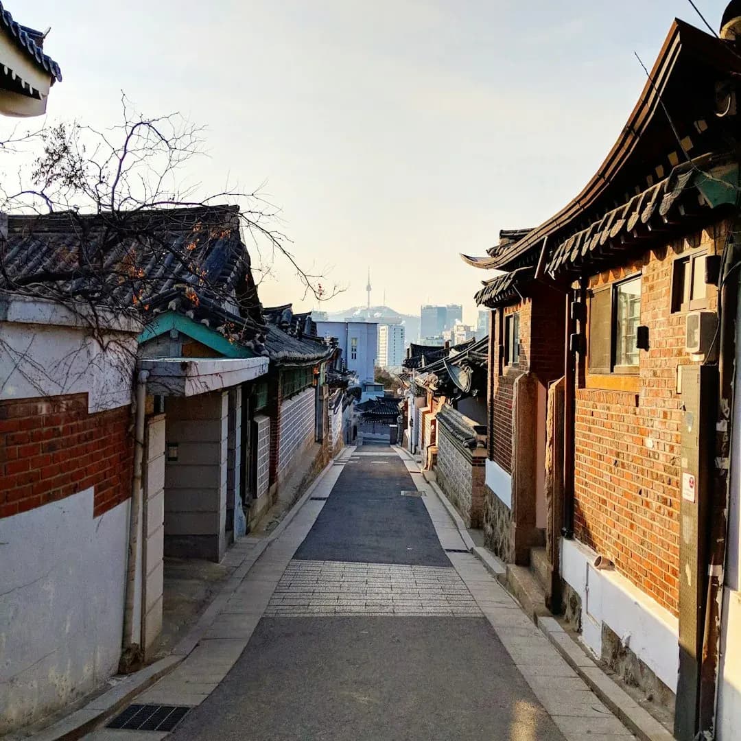 A wide illustration of Seoul at golden hour: Gyeongbokgung Palace in the foreground, the Han River winding through the city behind it, and the N Seoul Tower rising above a clear amber skyline.