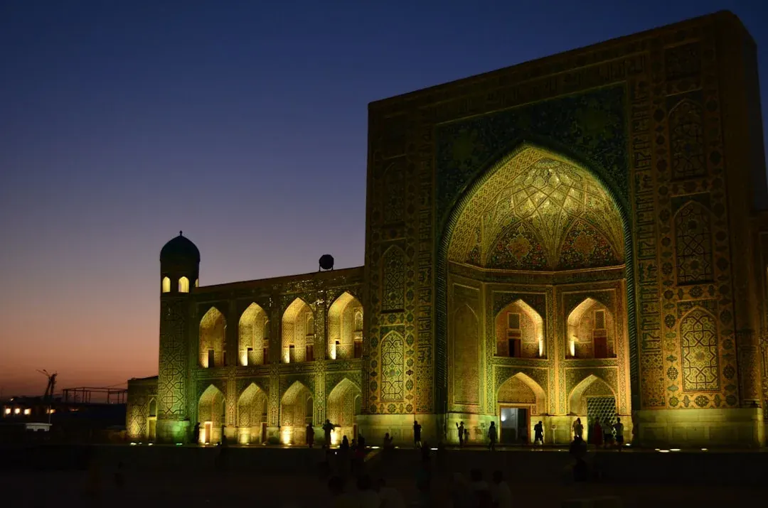 A warm illustration of Tashkent at golden hour, with the domes and tiled facade of the old city quarter glowing under a soft amber sky.