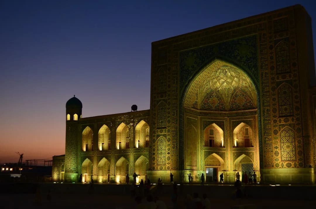 A warm illustration of Tashkent at golden hour, with the domes and tiled facade of the old city quarter glowing under a soft amber sky.
