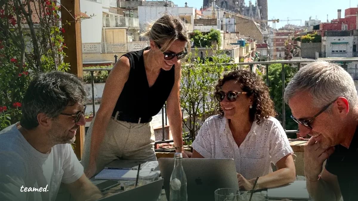 Four colleagues in conversation around a table on a sunny Barcelona rooftop, a small-group discussion like the HR Leaders Roundtables.