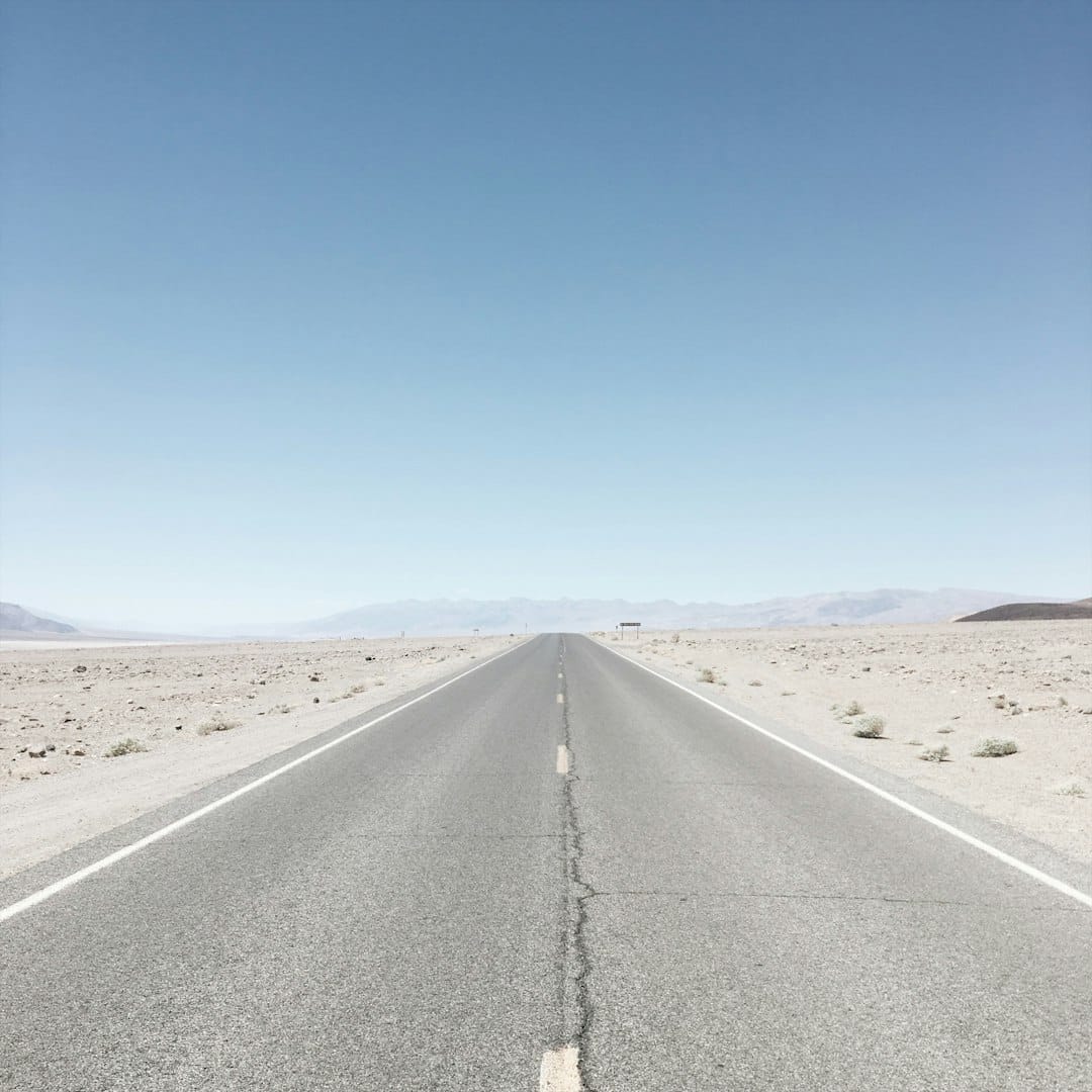 Nevada desert highway stretching to the horizon under open sky, warm afternoon light.