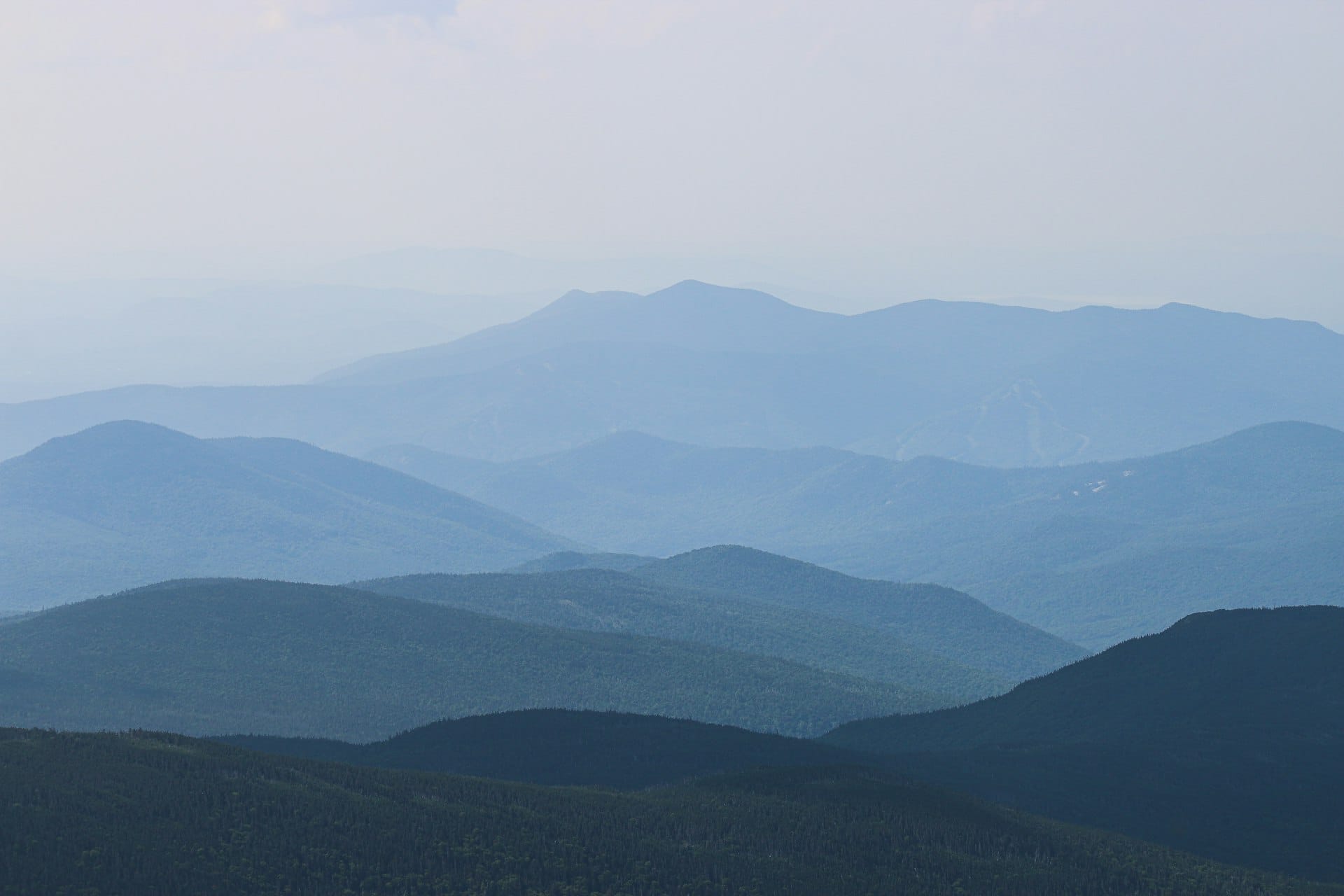 Autumn foliage across the White Mountains of New Hampshire, forested ridgelines in shades of amber and gold under a clear sky, a wide valley below.