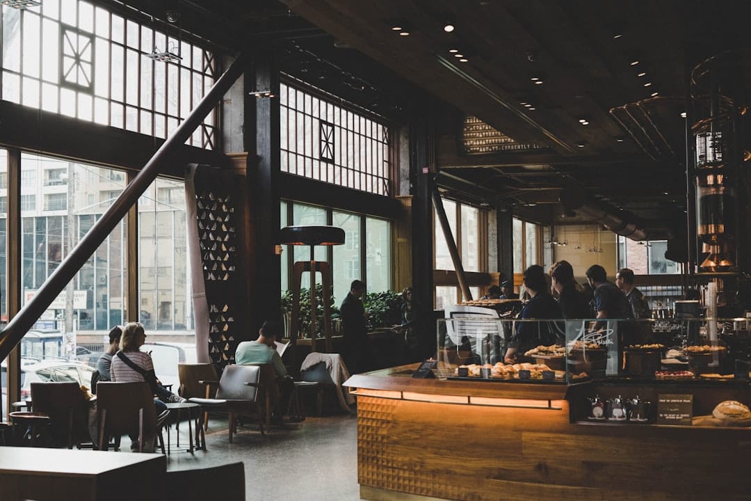 Two professionals in conversation over coffee at a cafe table, notebooks open, morning light through a window