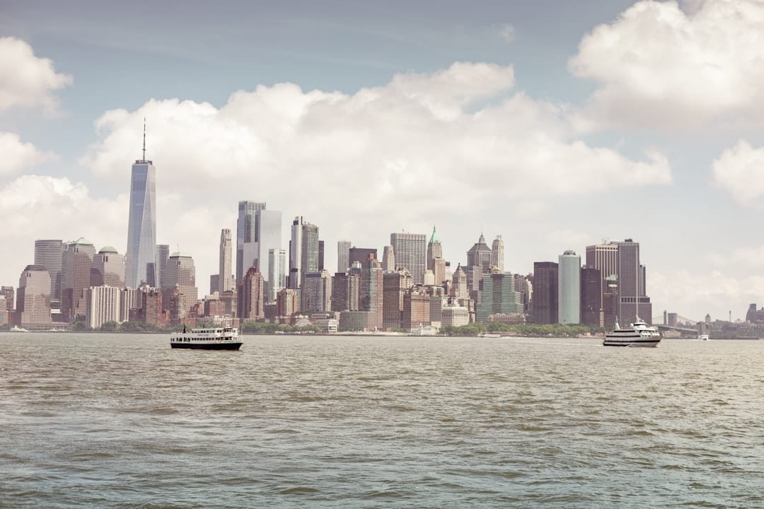 New York City skyline viewed from the water, the Manhattan towers rising under a wide sky with boats on the harbour below