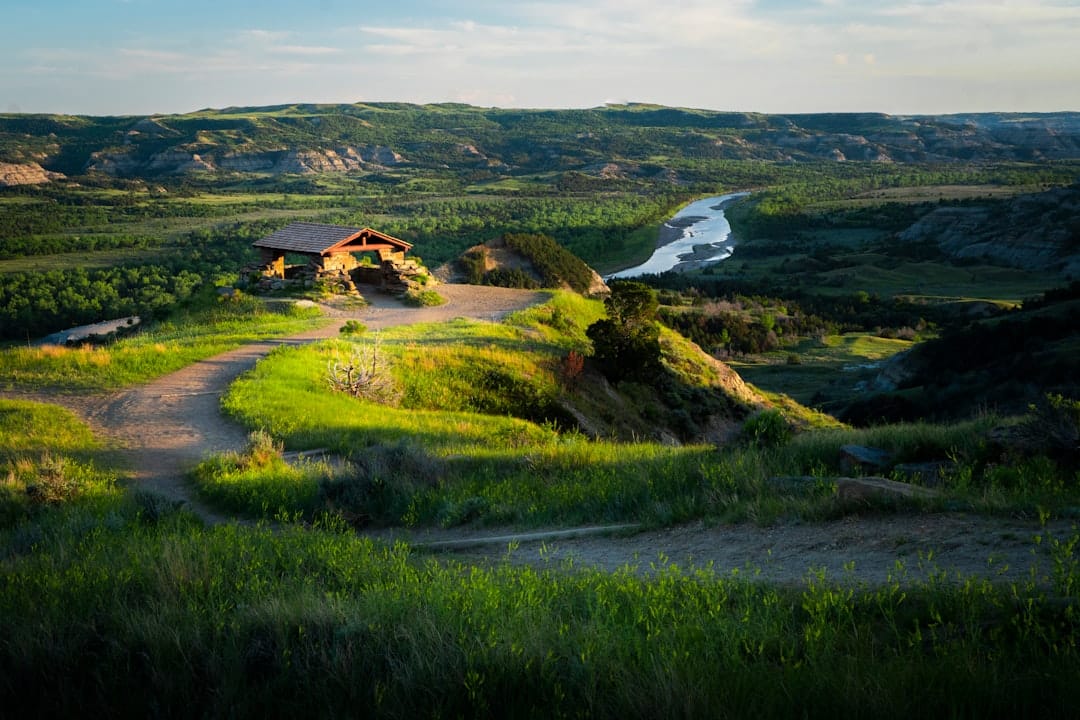 Wide landscape of the North Dakota plains under a broad open sky, golden light across the horizon, a distant farmstead visible in the open country.