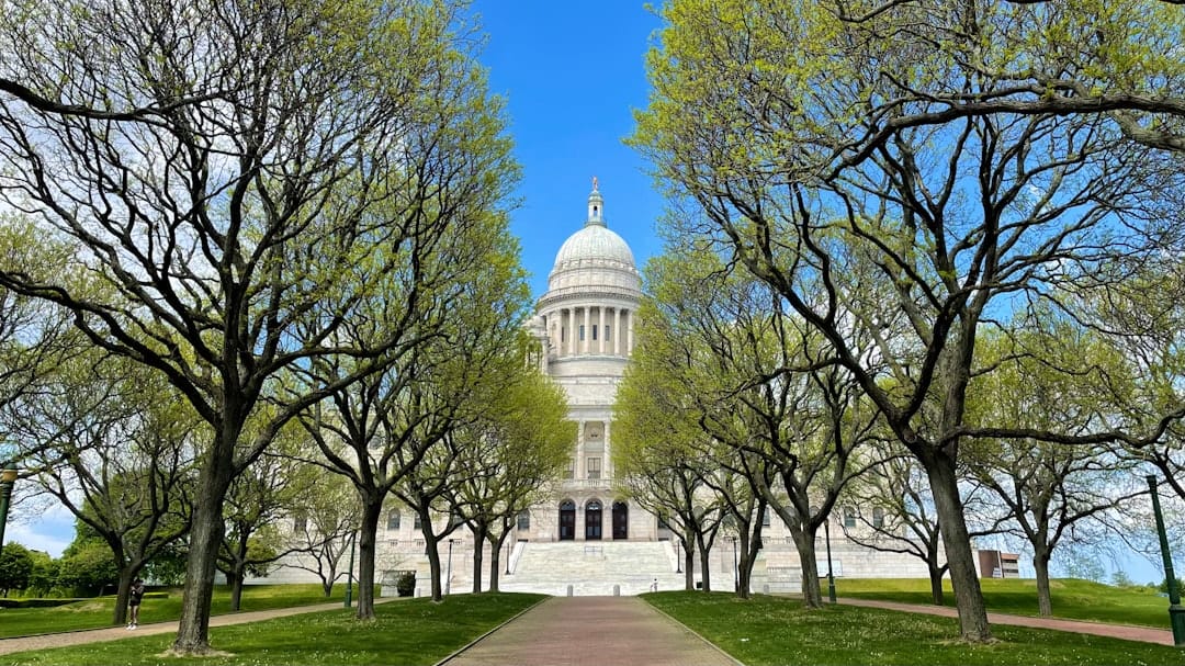 The Rhode Island State House dome rising above blooming trees in Providence on a clear day.