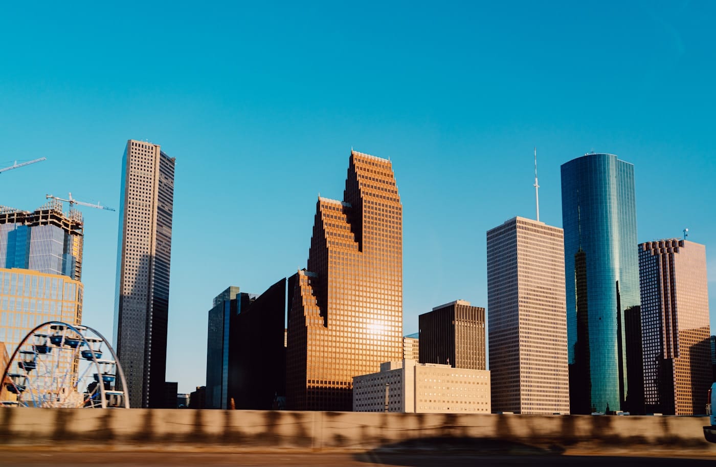Houston skyline at dusk reflected in Buffalo Bayou, with modern glass towers catching the last light against a deep-orange sky.