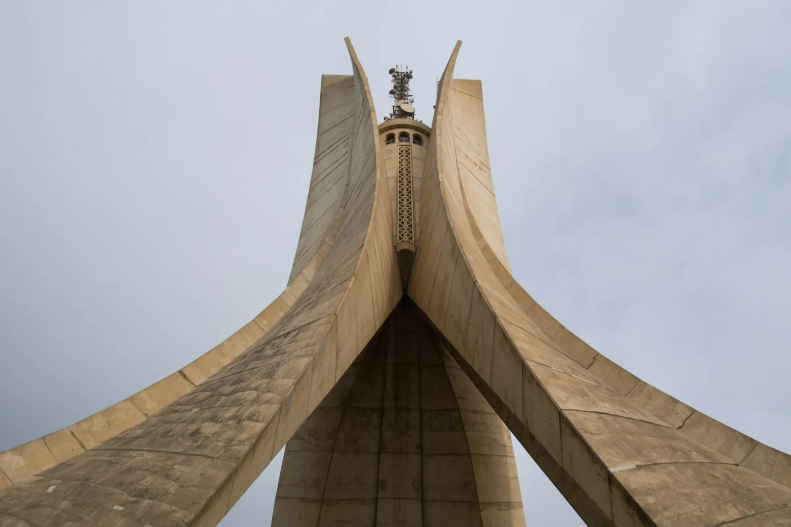 The Martyrs Memorial (Maqam Echahid) in Algiers, three concrete leaves rising to a point, seen from below against a pale grey sky.