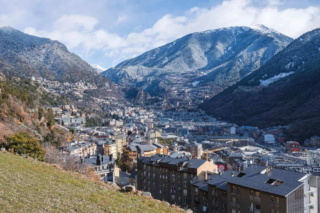 Andorra la Vella spread along a valley floor below snow-dusted Pyrenean peaks, with rows of apartment blocks in the foreground.