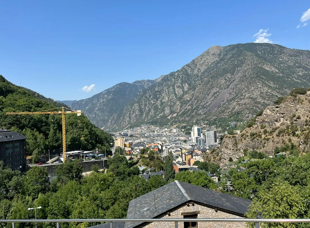 Escaldes-Engordany in a green valley, with a yellow construction crane and a slate roof in the foreground and mountains beyond.