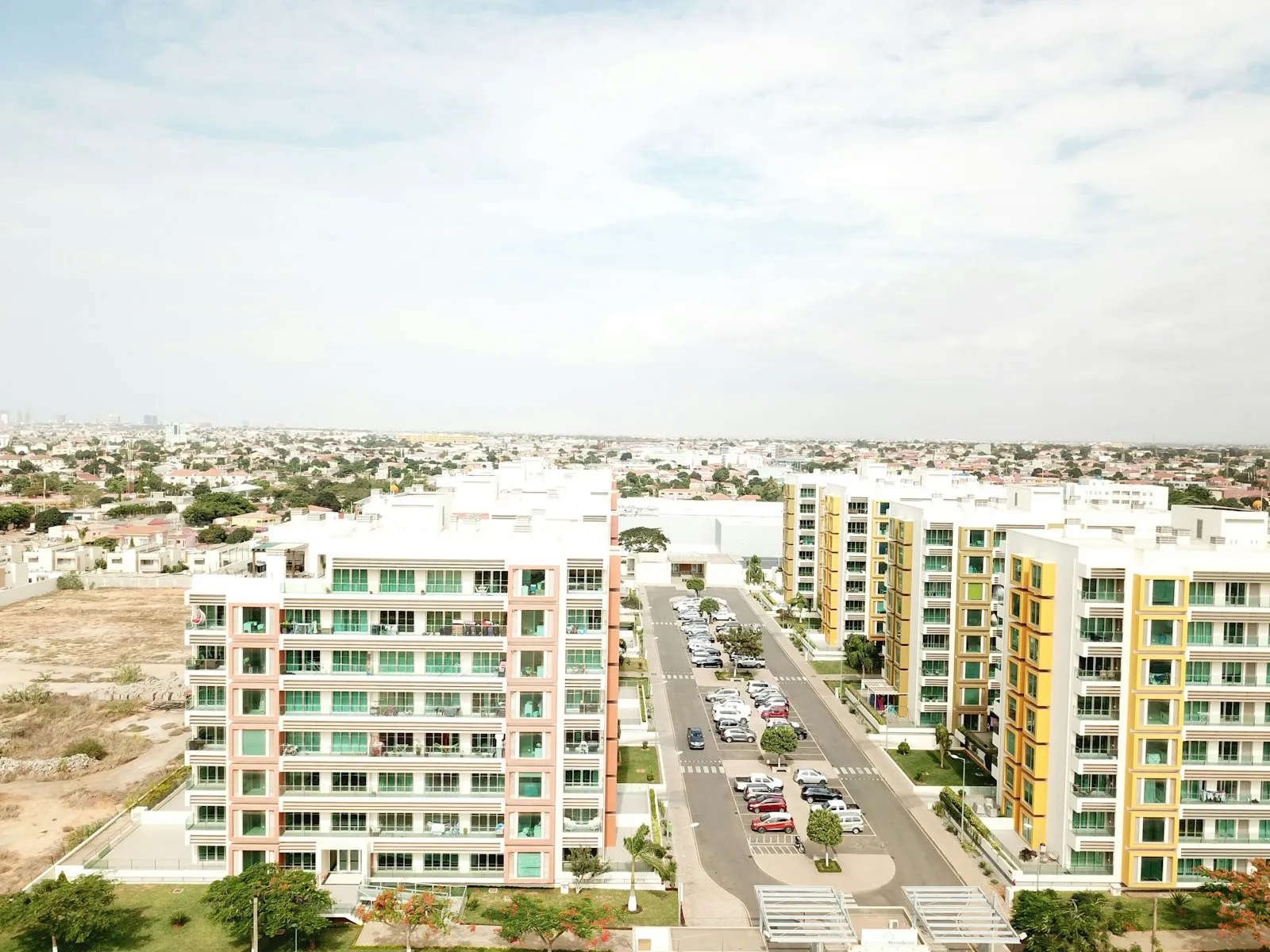 Apartment blocks in pastel colours along a wide street, with low houses and a flat horizon beyond, in an Angolan city.