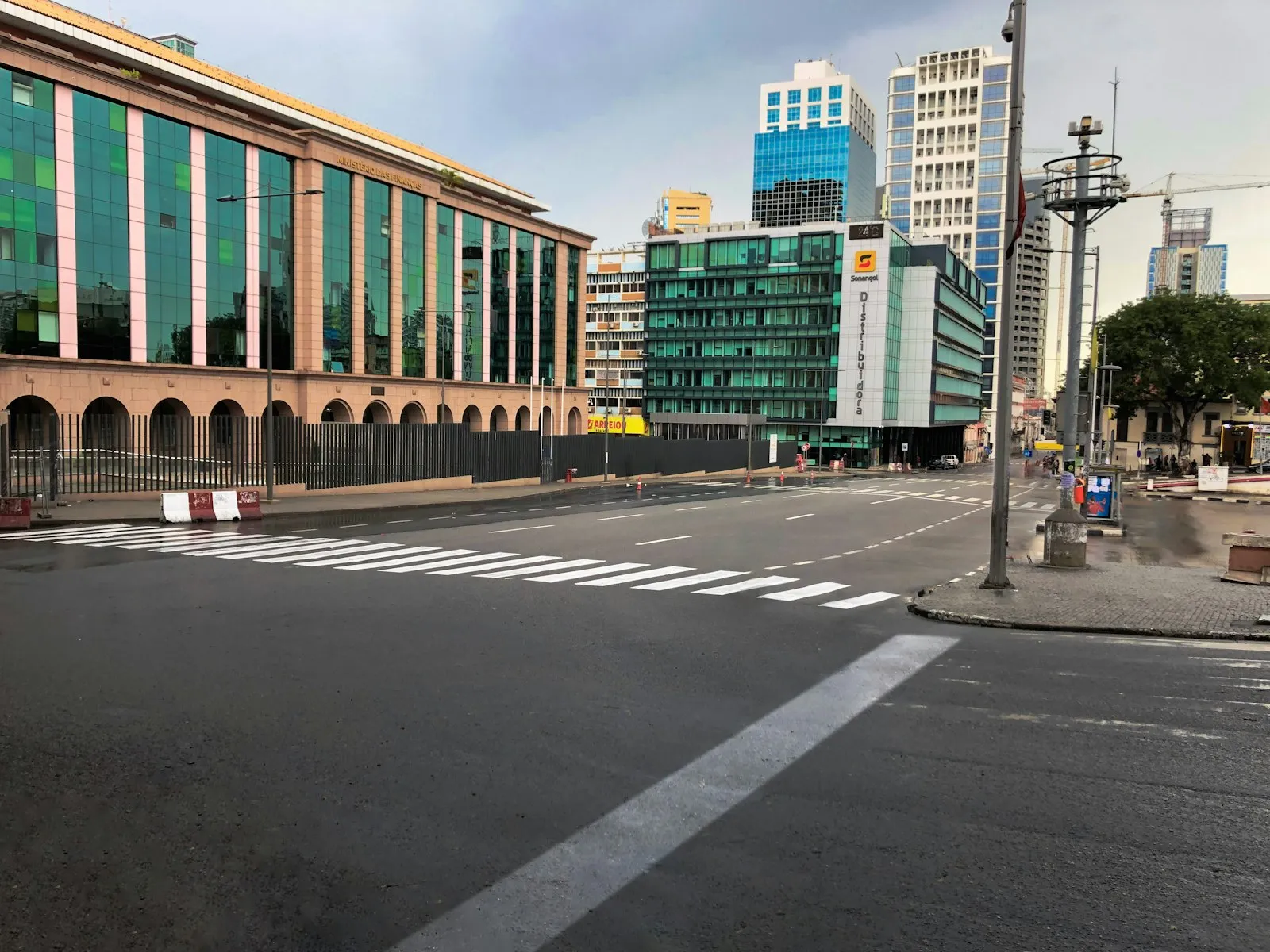An empty street crossing in Luanda, with glass-fronted office blocks and taller towers behind it under a pale sky.