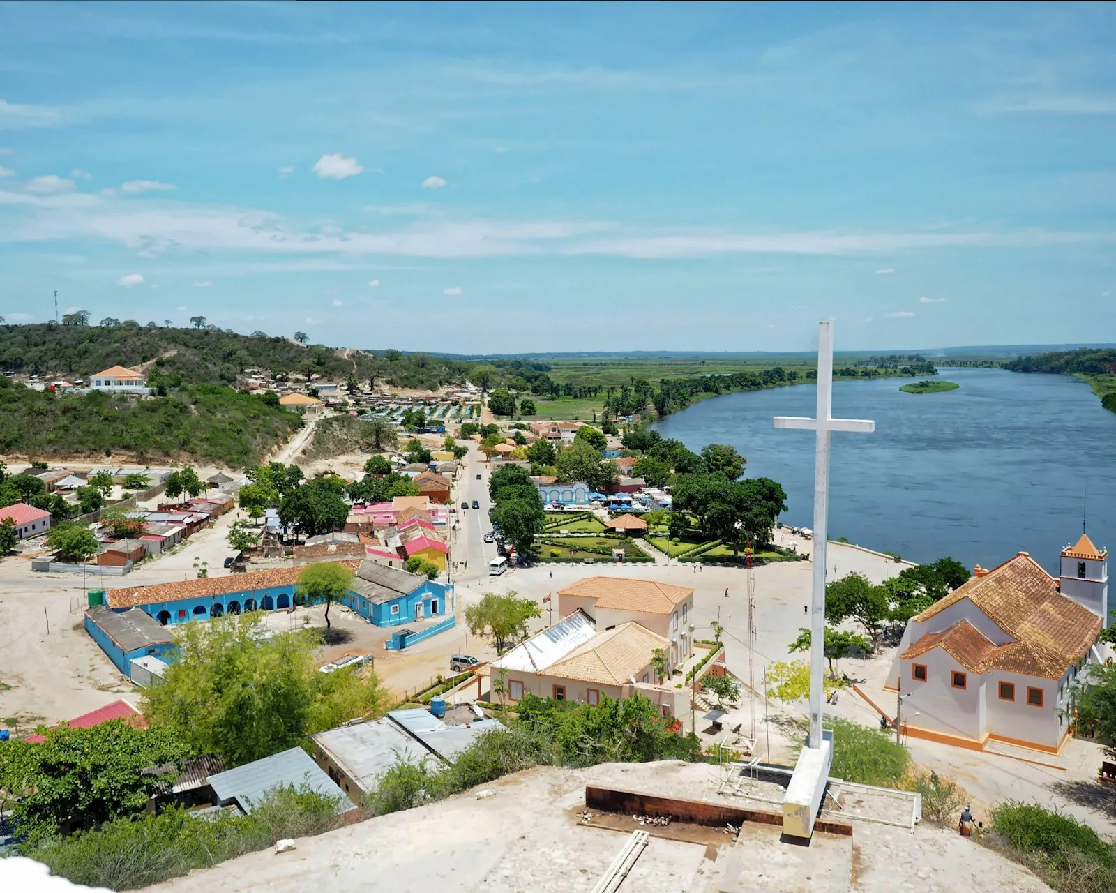 A riverside town in Angola seen from above: a white cross on a hill, low houses with red roofs and a wide river beyond.