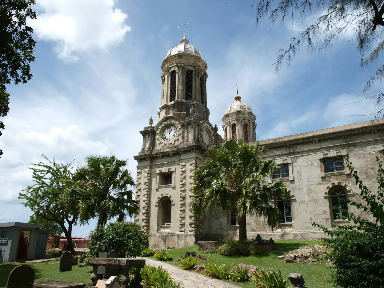 The twin-towered stone facade of St John's Cathedral in Antigua with palm trees in front under a bright sky.