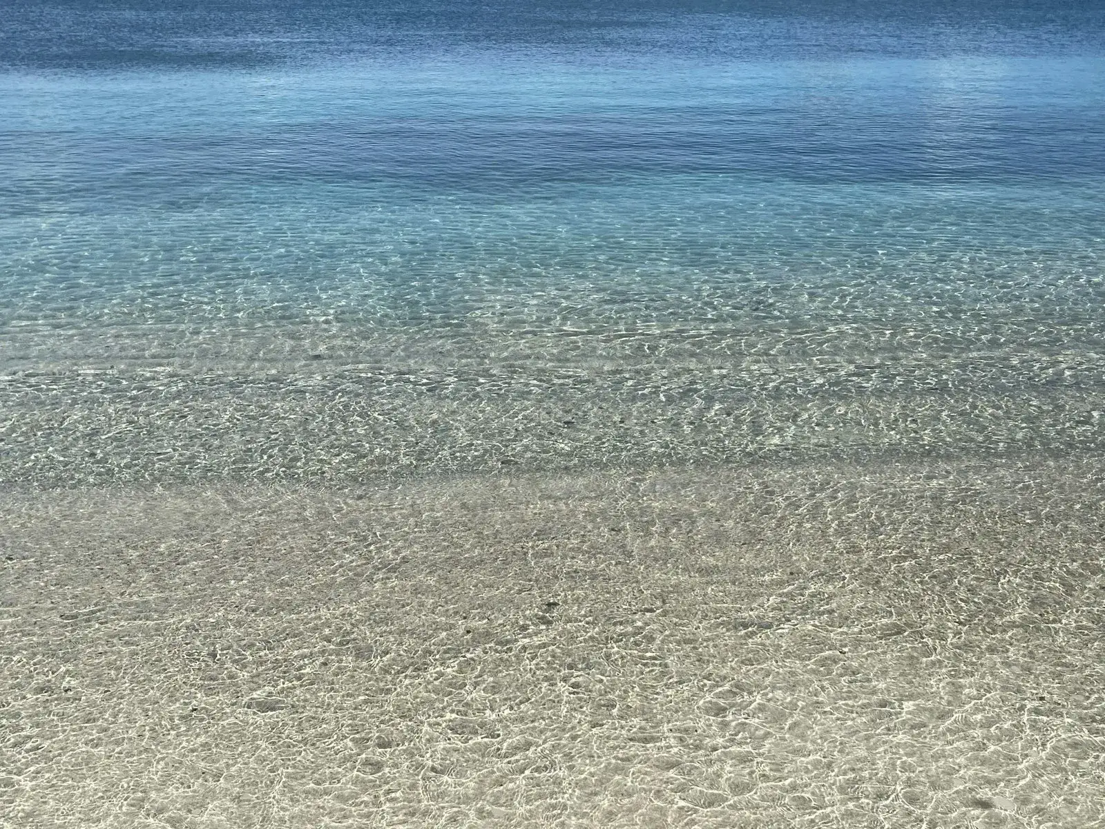 Clear, shallow turquoise water over pale sand at the edge of the sea in Antigua and Barbuda.