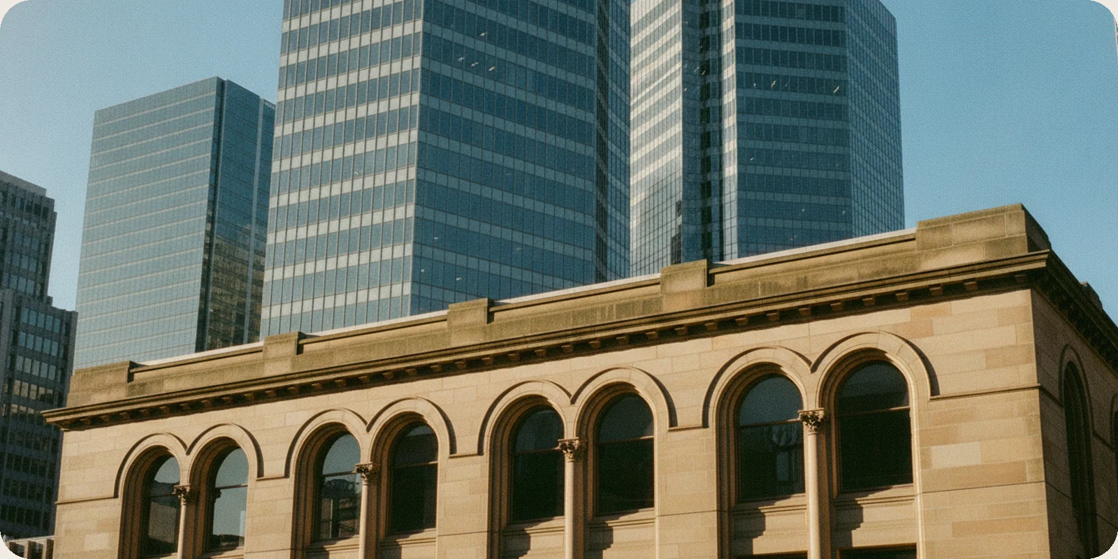 An old sandstone building with arched windows in Sydney's business district, with modern glass office towers rising behind it under a clear blue morning sky.