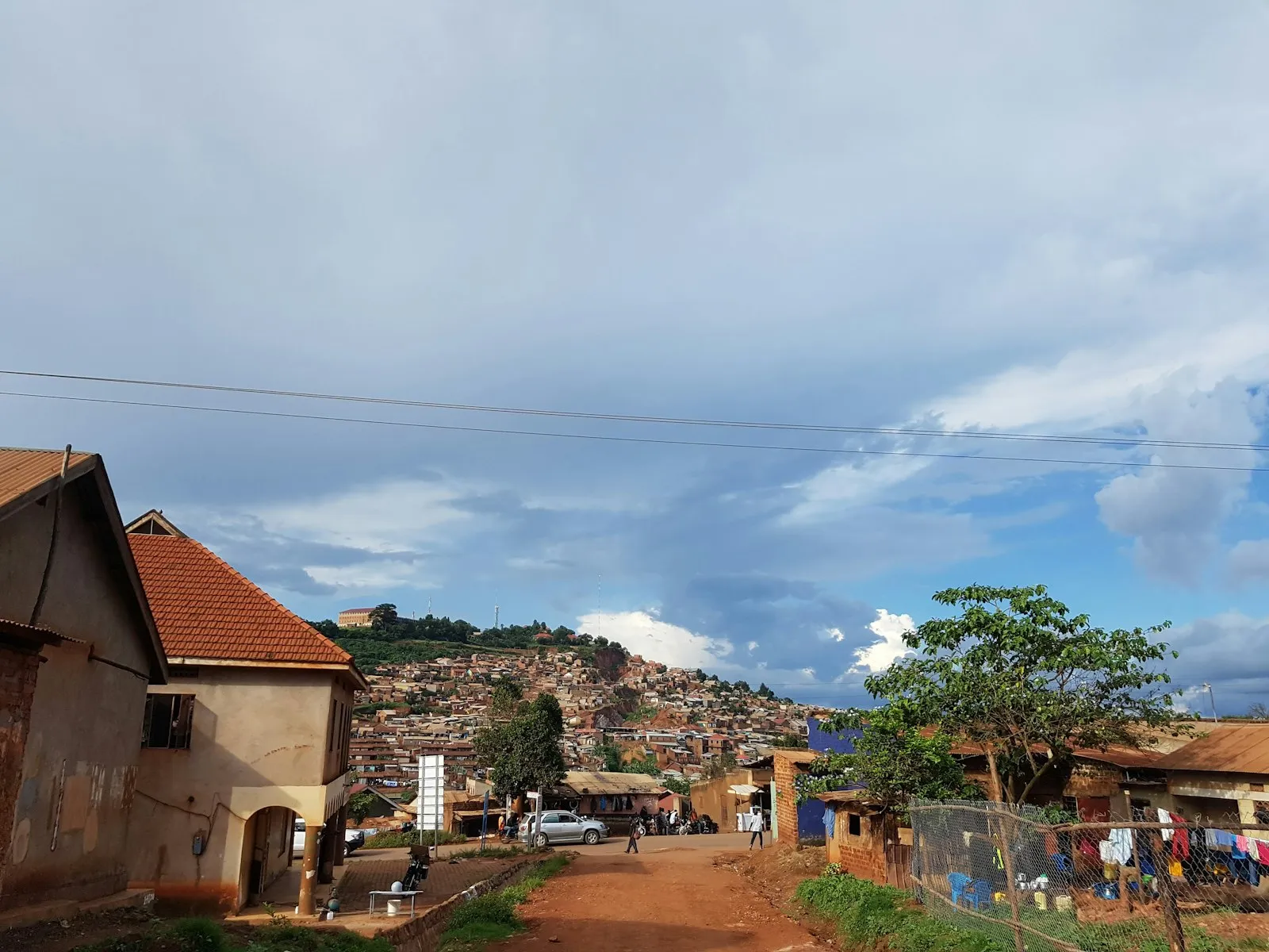 Houses with red-tiled roofs among green trees on a hillside under a blue sky with white clouds in Burundi.