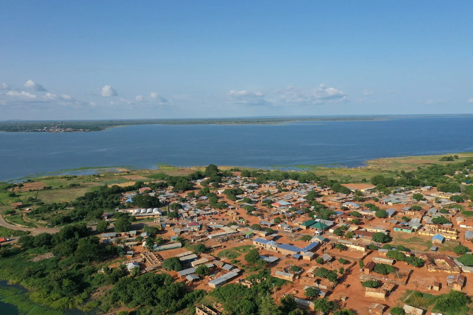 An aerial view of a red-roofed village on a shore beside a wide stretch of water under a blue sky in Burundi.