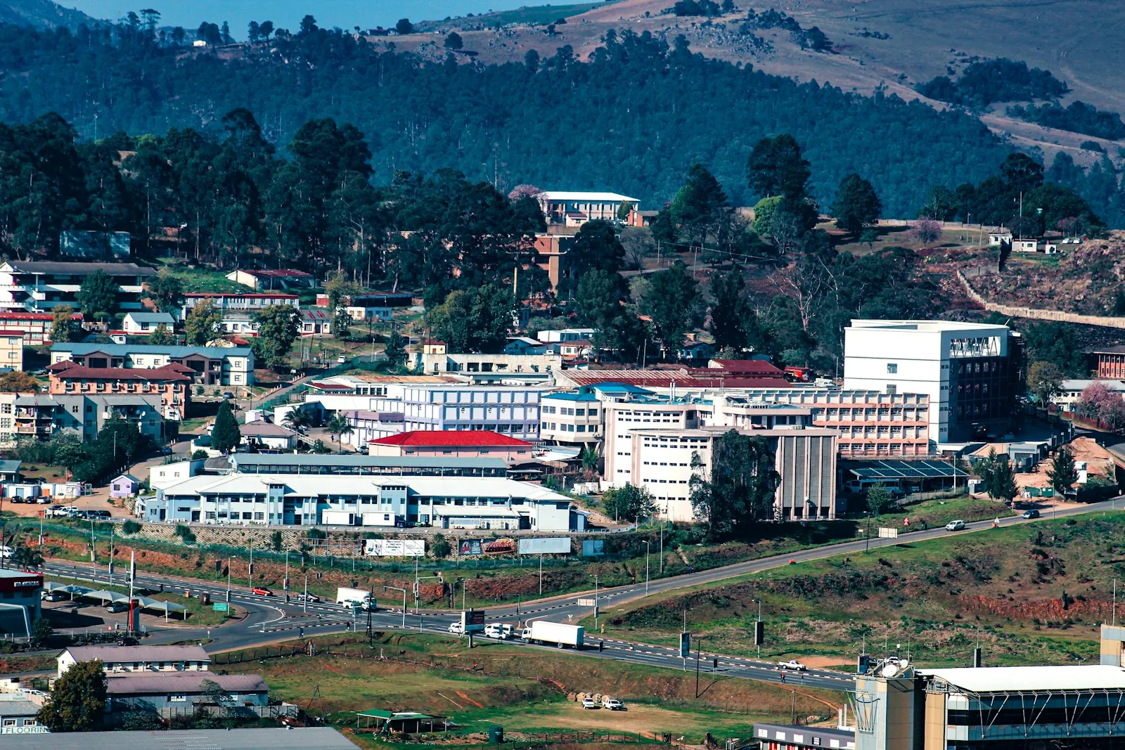 White office blocks and red roofs spread across a wooded hillside, with a road running through the valley below.