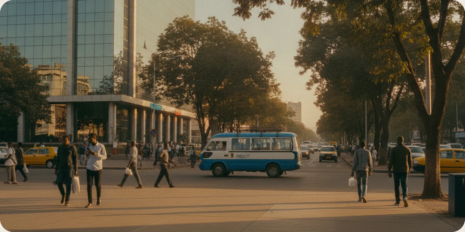 A tree-lined street in Addis Ababa, Ethiopia, in late afternoon light, with people walking and a blue and white minibus taxi passing a glass office building.
