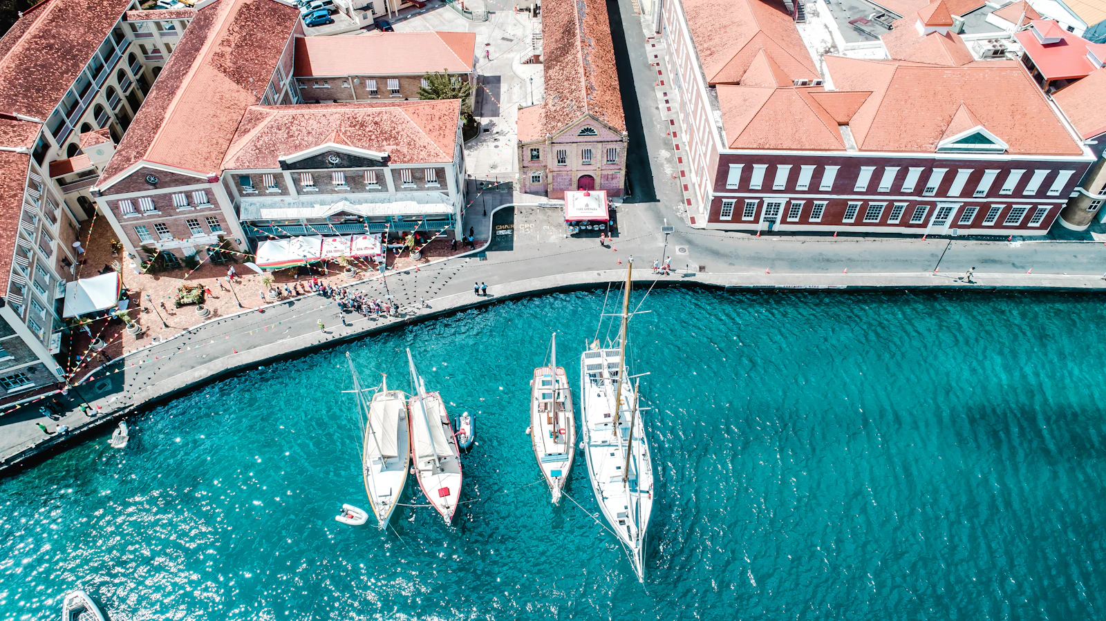Sailing boats moored in a turquoise harbour beside red-roofed Georgian buildings on the quay in St. George's, Grenada.