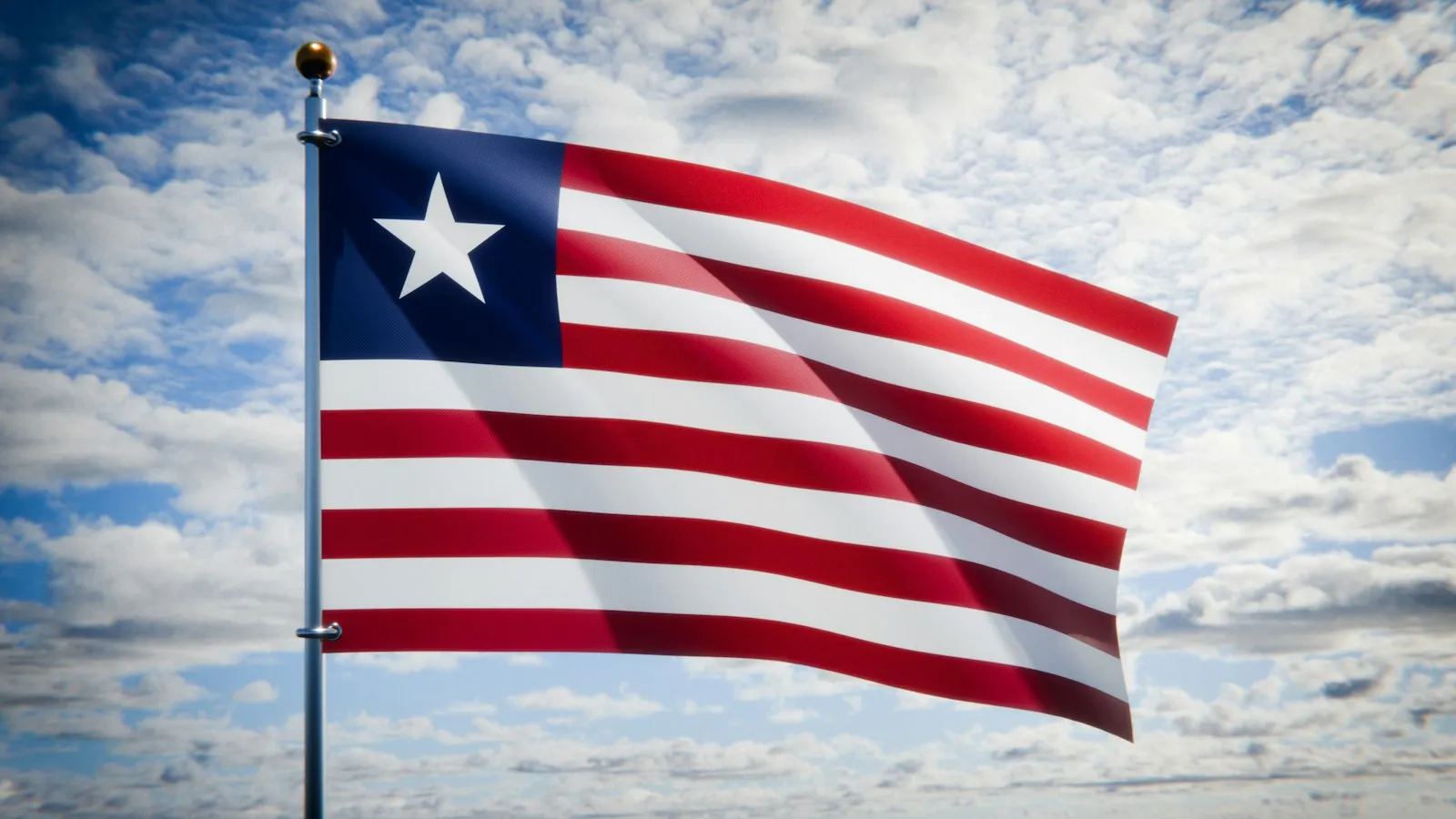 The red and white striped flag of Liberia, with a white star on a blue square, flying against a cloudy sky.