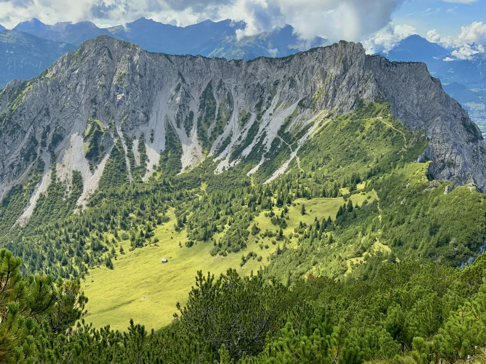 A steep, forested limestone ridge above Vaduz at the Fuerstensteig, with clouds lying over the valley below.