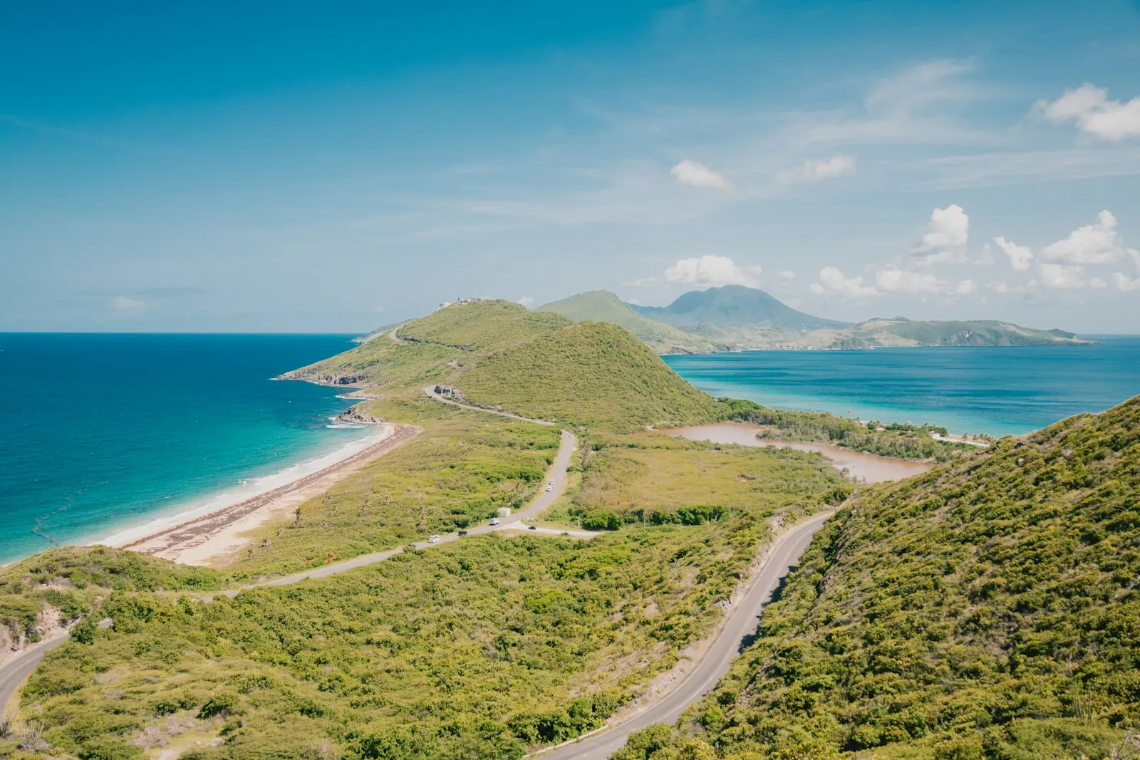 Winding paths along the green hills of the south-east peninsula of Saint Kitts, with turquoise sea on both sides and a distant island peak.