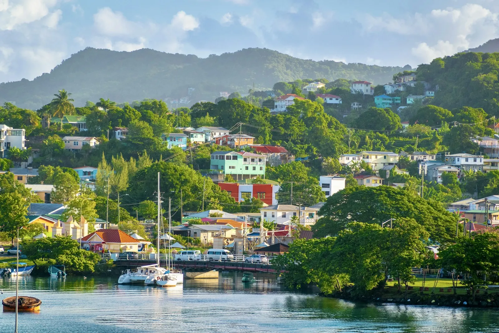 Sailing boats moored in a river mouth beside a hillside town of colourful houses on Saint Lucia.