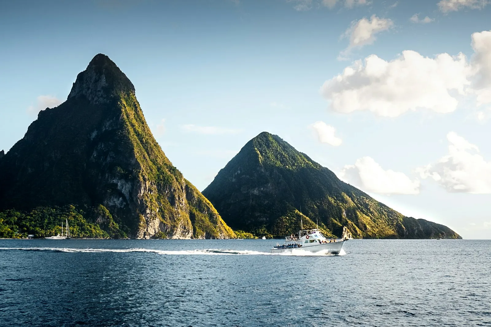 The two Piton peaks rising from the sea off Saint Lucia, with a white yacht on the water in front.