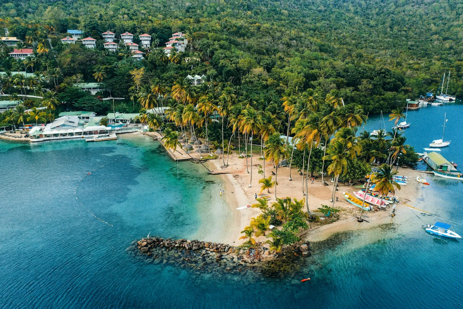 An aerial view of a sheltered bay with a palm-covered sand spit, moored boats and green hills in Saint Lucia.