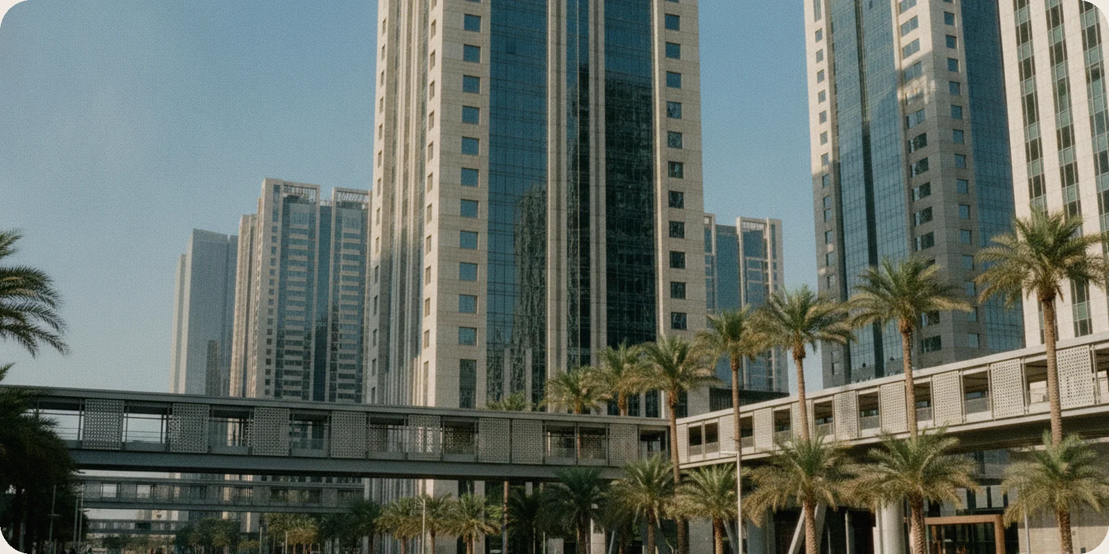 Modern glass and stone office towers in Riyadh's King Abdullah Financial District, with shaded walkways and palm trees under a clear blue morning sky.