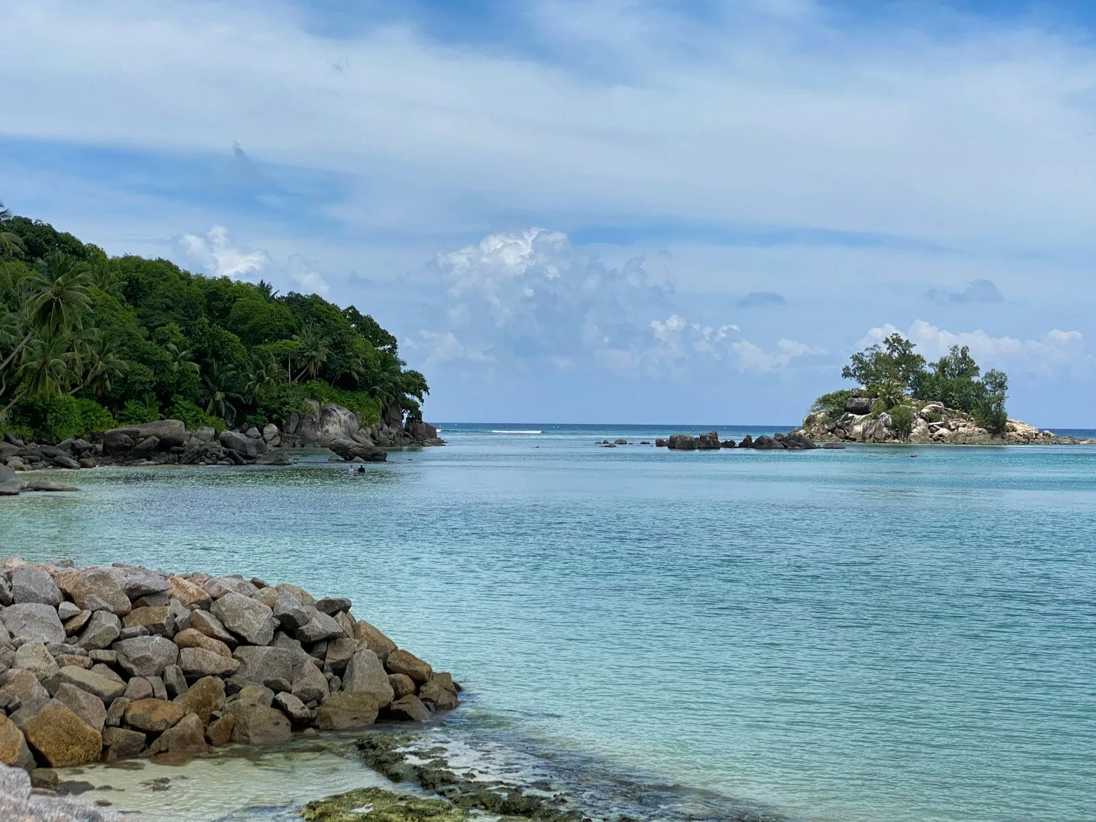 A rocky green headland and a small island across turquoise water at Anse Royale on the island of Mahe.