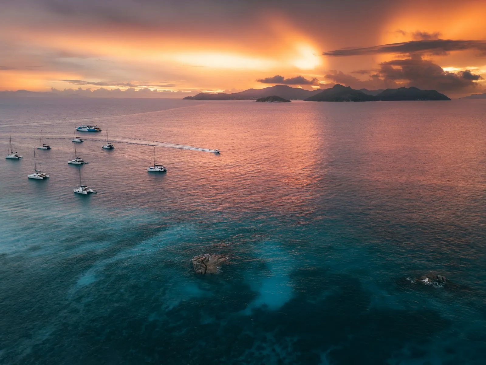 Moored boats and an island silhouette against an orange sunset over the sea off La Digue, Seychelles.