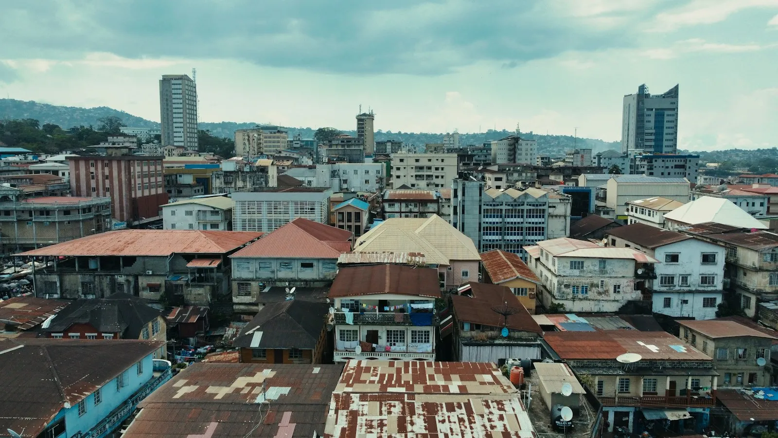 Freetown rooftops and streets seen from a tall building, with two towers rising above the town and hills in the distance.