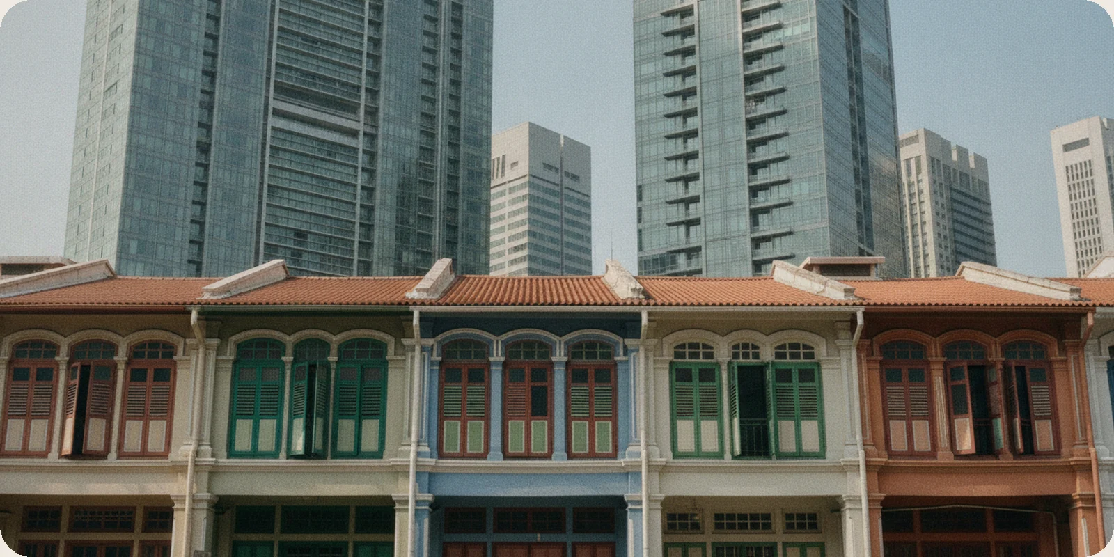 A row of restored two-storey shophouses with painted shutters in Singapore's Telok Ayer, with the office towers of the business district rising behind them in clear morning light.